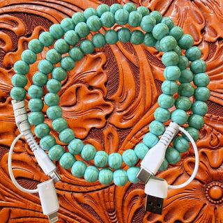 Light turquoise beaded charging cable with USB-A, USB-C, and Lightning connectors on brown tooled leather background.