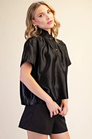 Black stand collar button placket short sleeve shirt with gold buttons, worn with black shorts.