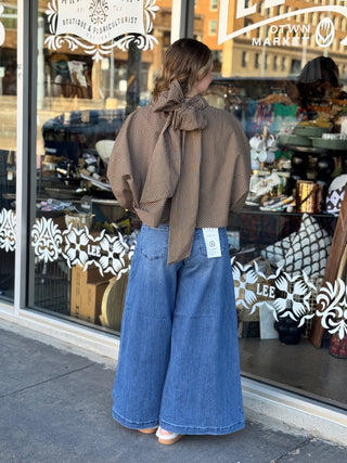 Brown and tan striped satin blouse with large back bow tie detail, paired with wide-leg jeans.