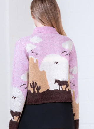 Pink knit cardigan featuring Western desert scene with horses, cacti, mesas, and clouds on back.