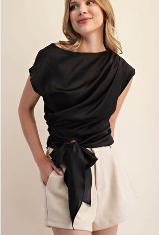 Black boat neck blouse with side ruching and waist tie, paired with cream shorts.