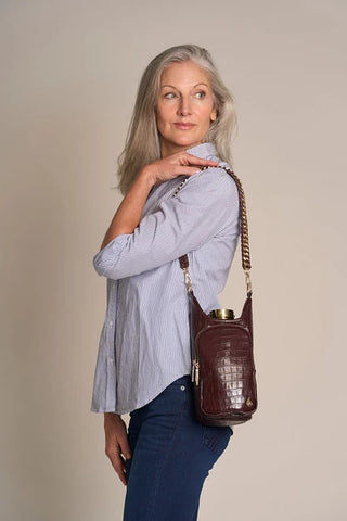Woman wearing a merlot faux crocodile crossbody HydroBag with gold chain strap over striped shirt.