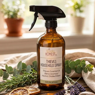 Amber glass spray bottle of Simply Honest Co. Thieves Household Spray surrounded by eucalyptus, lavender, rosemary, and dried