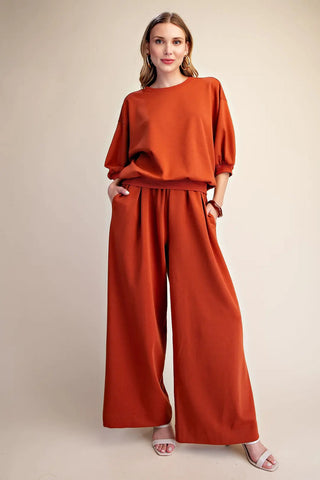 Rust orange pullover sweatshirt with bubble sleeves, crew neck, and ribbed hem, styled with matching wide-leg pants.