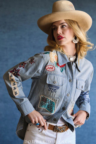 Woman wearing light blue striped denim jacket with embroidered patches, stars, and American flag detail.