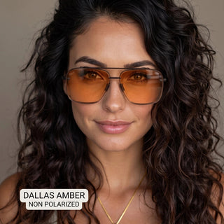 Woman wearing Dallas aviator sunglasses with amber orange lenses and slim gunmetal frames, curly dark hair.