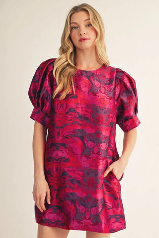Red and purple floral jacquard mini dress with puff sleeves and round neckline on blonde model.