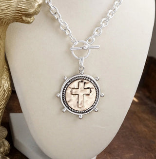 Silver-tone chain necklace featuring circular cross coin pendant with decorative border and front toggle closure.