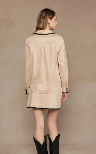 Beige suede shirt with black contrast embroidered trim, long sleeves, worn over matching mini skirt with cowboy boots.