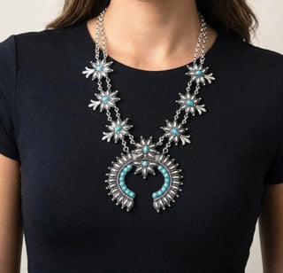 Silver squash blossom necklace with turquoise gemstone accents and floral details worn on model.