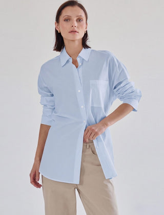 Light blue oversized button-down shirt with white chest pocket, spread collar, and rolled sleeves.