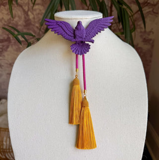 Purple 3D eagle bolo tie with spread wings, fuchsia cords, and hanging golden yellow tassels.