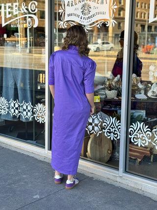 Purple midi shirt dress with ruffle collar and puff sleeves, shown from behind on model outside boutique.