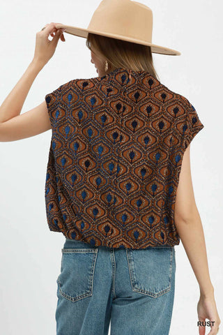 Rust brown velvet mock neck cap sleeve top with blue and navy geometric floral embroidered pattern, worn with jeans.