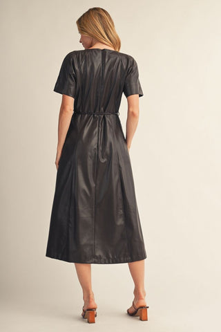 Black faux leather midi dress with short sleeves, seam detailing, and tie waist, styled with brown heels.