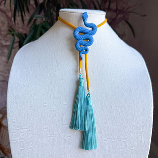 Blue coiled snake bolo tie pendant on golden yellow cord with dual peacock blue tassels displayed on white bust.