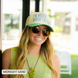 Woman wearing round polarized sand-tinted sunglasses with brown lenses, paired with a green striped trucker hat outdoors.
