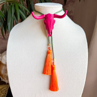 Hot pink longhorn skull bolo tie necklace with olive green cord and orange tassel pendants on display bust.