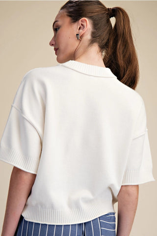 White knit sweater with elbow-length sleeves, ribbed trim, and seam detail, worn from behind.
