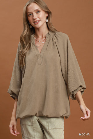 Mocha balloon sleeve split neck blouse with smocked neckline, worn with light khaki pants and pearl earrings.