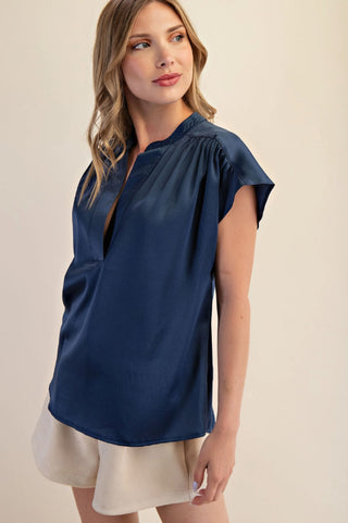 Navy blue satin blouse with V-neckline, gathered shoulders, and cap sleeves, styled with cream shorts.