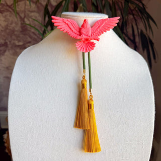 Pink eagle bolo tie with olive green cord and two golden yellow silk tassels on white bust display.