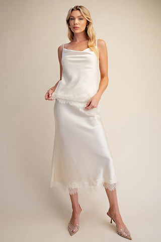 Ivory satin cami top with cowl neckline, thin straps, and delicate lace hem trim detail.