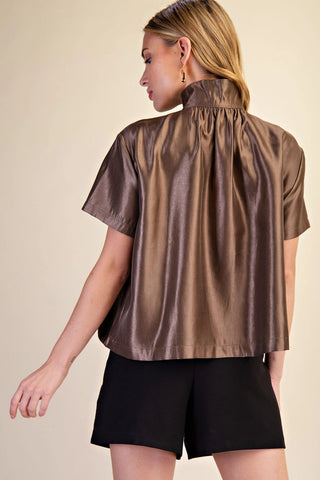 Bronze metallic short sleeve shirt with stand collar, gathered back detail, worn with black shorts.
