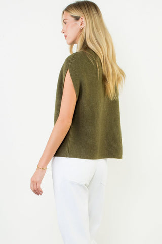 Olive green sleeveless mock neck knit sweater top with open sides, paired with white jeans.