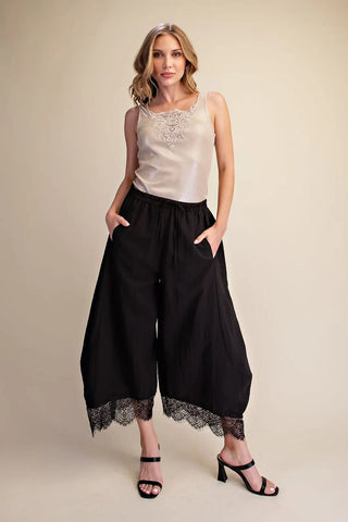 Black cropped balloon pants with lace hem trim, elastic waistband, and relaxed wide-leg silhouette.