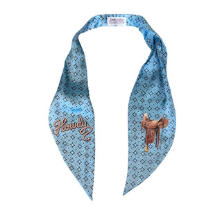 Light blue chambray bandana scarf with dark floral print, "Howdy" script embroidery, and western saddle graphic.