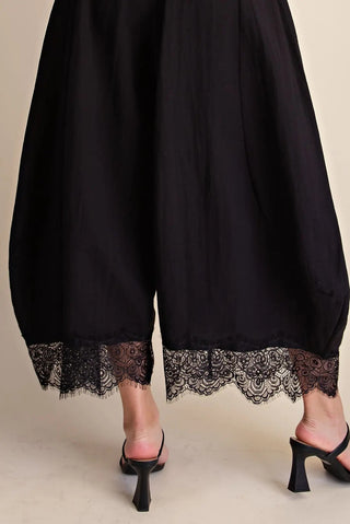 Black cropped balloon pants with intricate lace trim hem detail, styled with black heeled mules.