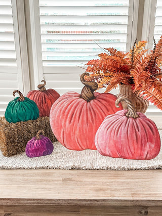 Two large velvet pumpkins in coral red and dusty pink displayed on a table with fall decor.