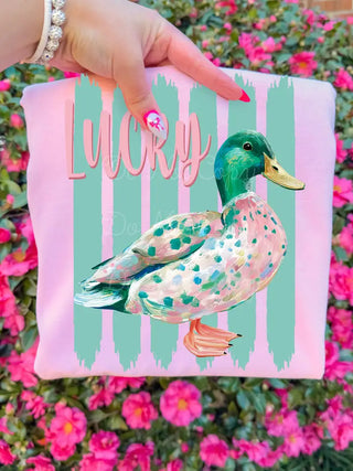 Pink "Lucky Duck" graphic tee featuring a painted mallard duck with teal stripes, held against pink flowers.
