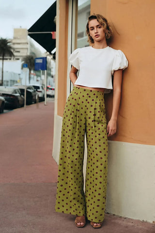 Olive green wide-leg pleated pants with burgundy polka dots, high-waisted, full-length, paired with white crop top.