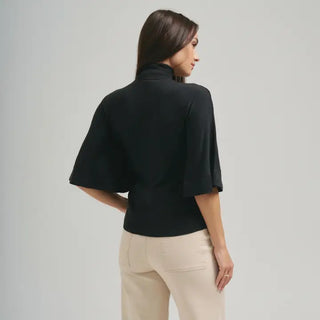 Woman wearing a black turtleneck half-sleeve cropped sweater with wide sleeves, paired with beige pants.