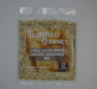 Small clear packet of Tastefully Gourmet Garlic Bacon Ranch Cracker Seasoning Mix with herb-flecked powder visible through pa
