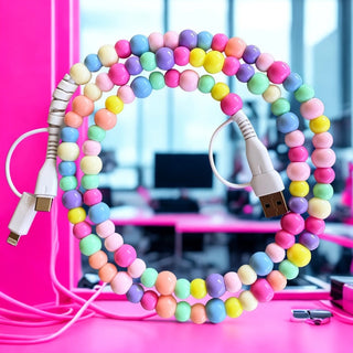 Pastel multicolor beaded 4-in-1 charging cable coiled on pink desk with USB-A and Lightning connectors visible.