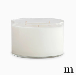 Large white three-wick candle in clear glass vessel, unlit, clean minimal presentation.