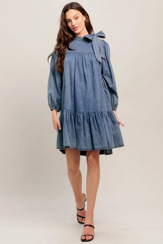 Acid washed lightweight denim mini dress with bow detail, tiered ruffle hem, and long balloon sleeves.