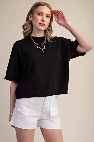 Black cropped mock-neck sweater with elbow-length sleeves and ribbed hem detailing, styled casually.