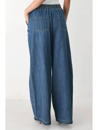 Wide-leg washed blue denim pants with elastic waistband and back patch pockets, rear view.