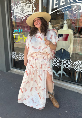 White cowboy boot print short sleeve top with front placket detail, worn with matching maxi skirt and straw hat.