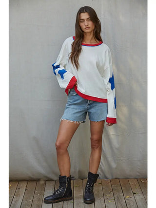 White knit cotton long sleeve top with blue star details and red trim, styled with denim shorts.