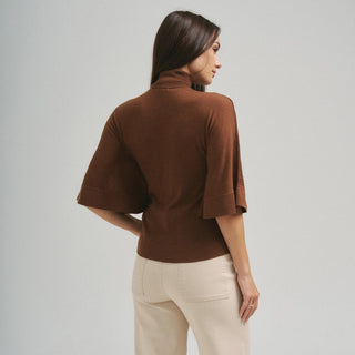 Brown turtleneck half-sleeve sweater with wide flutter sleeves, worn with cream pants, back view.