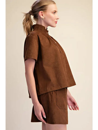Brown suede stand collar short sleeve cropped shirt worn with matching brown shorts, side view.