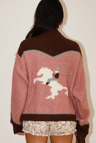 Pink and brown knit sweater featuring white rodeo cowboy on bucking horse intarsia graphic on back.