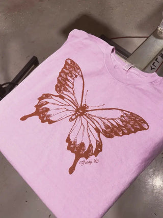 Pink crewneck t-shirt featuring a rust brown vintage-style butterfly graphic with "Grady Ln" script text.