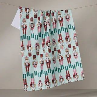 Mint green tea towel featuring rows of colorful nutcracker soldiers in pink, red, and brown tones.