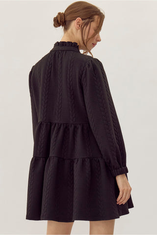 Black textured cable-knit tiered mini dress with frilled neckline and long sleeves, back view.
